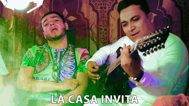 a man playing a guitar next to another man with the words la casa invita written below them