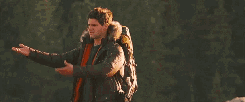 a man with a backpack is standing in the woods with his arms outstretched