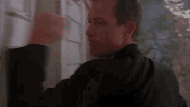 a man in a black suit is standing in front of a door and knocking on it .