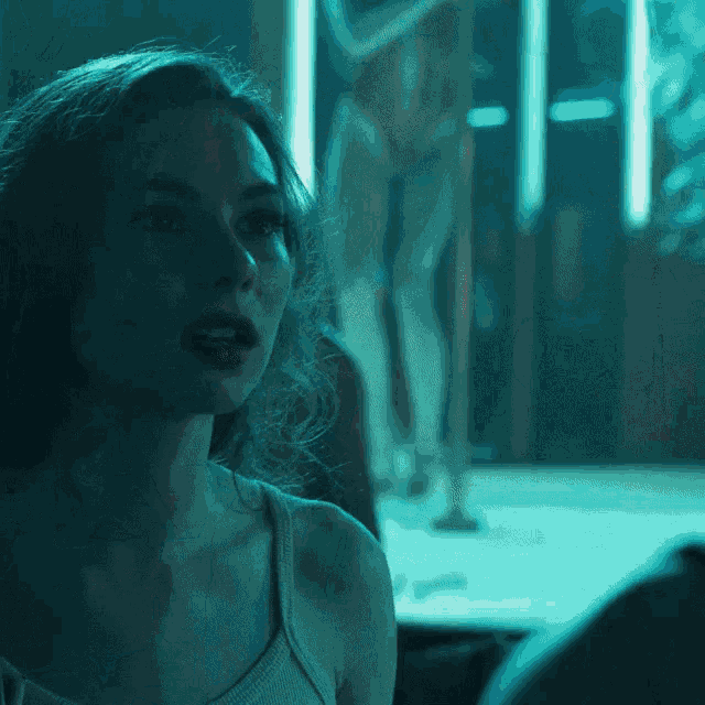 a woman in a tank top looks at a pole dancer in the background