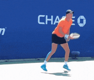 a man in an orange shirt is holding a tennis racquet in front of a blue wall that says chase