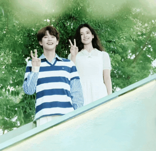 a man in a blue and white striped shirt stands next to a woman in a white dress giving a peace sign