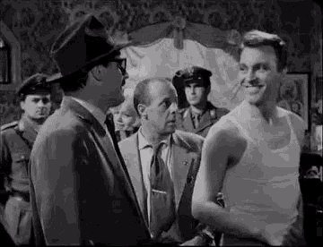a group of men are standing around a man in a tank top .