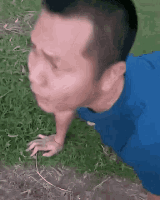 a man in a blue shirt is doing push ups in the grass