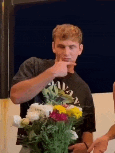 a man in a black shirt is holding a bouquet of flowers in his hand .