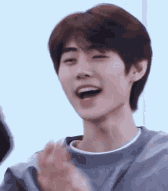 a young man is smiling and clapping his hands while wearing a gray sweater .