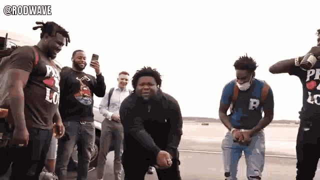 a group of men are standing on a street and one of them is wearing a shirt that says rodwave