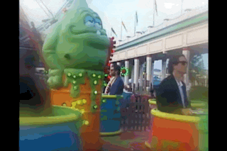 a group of people are riding a carnival ride with a green monster in the background