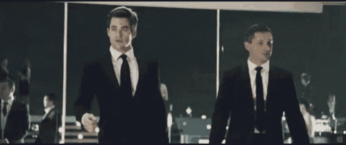 two men in suits are standing next to each other in front of a window
