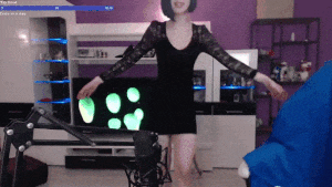 a woman in a black dress is dancing in front of a microphone in a living room