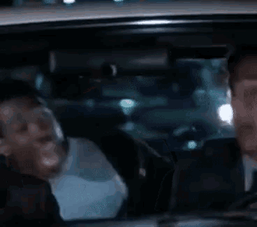 two men are sitting in a car at night and talking .