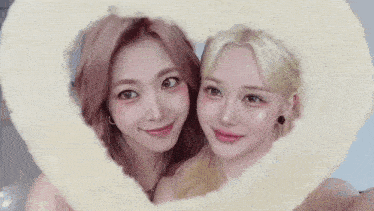 two women are taking a selfie with a heart shaped frame .