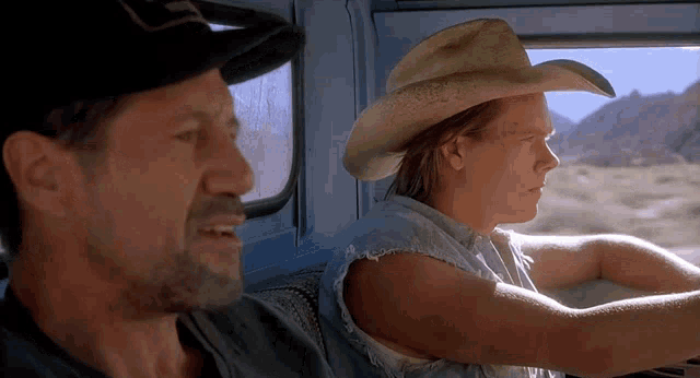 a man wearing a cowboy hat is sitting next to another man in a car .