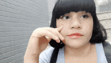 a woman with short black hair looks at the camera with her hand on her face