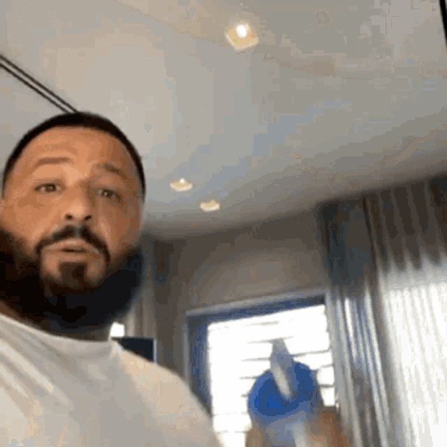 a man with a beard and a white shirt is standing in a room .
