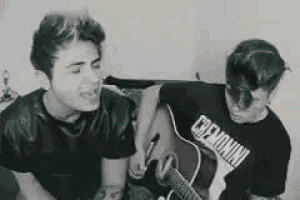 two young men are singing and playing guitars .