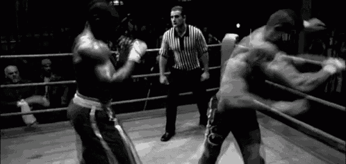 two men are boxing in a ring with a referee in the background .