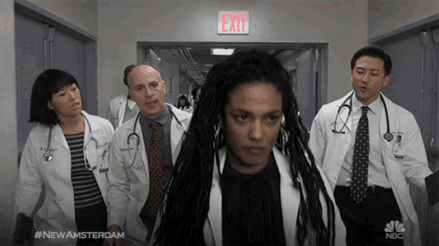 a group of doctors are walking down a hallway with an exit sign