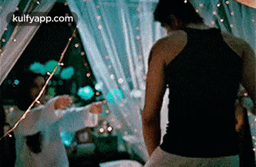 a man in a black tank top is standing in front of a woman in a white dress .
