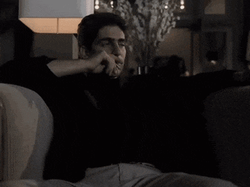 a man is sitting on a couch smoking a cigarette while watching tv .