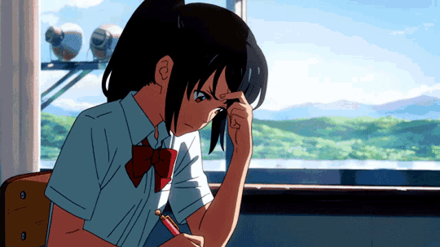 a girl in a school uniform is sitting in front of a window and writing in a notebook