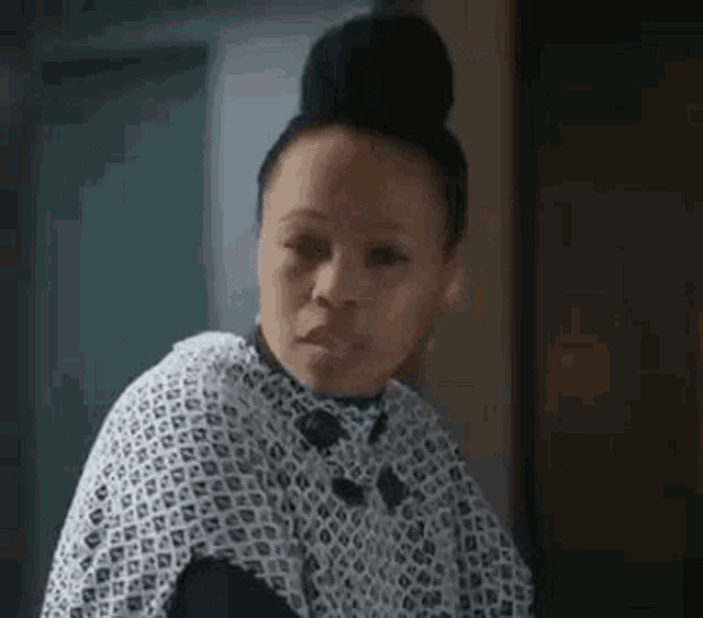 a woman with a bun on her head is wearing a white and black dress and looking at the camera .