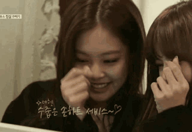 two girls are looking at themselves in a mirror and one of them is smiling .