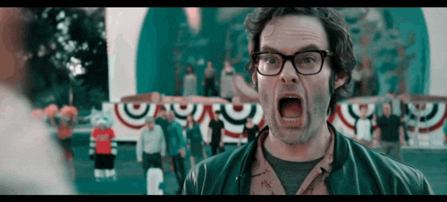 a man wearing glasses is screaming with his mouth open in front of a crowd of people .