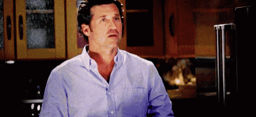 a man in a blue shirt is standing in a kitchen looking at the camera .