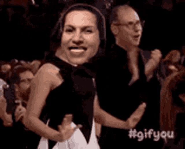 a woman in a black dress is dancing in front of a crowd .