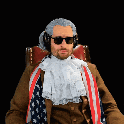 a man in a wig and sunglasses is sitting in a chair with an american flag around his neck