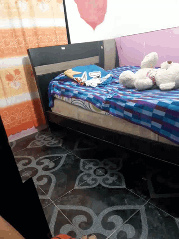 a teddy bear is sitting on a bed with a blue and purple blanket