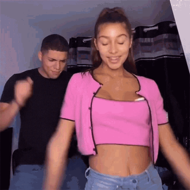 a man and a woman are dancing together and the woman is wearing a pink crop top
