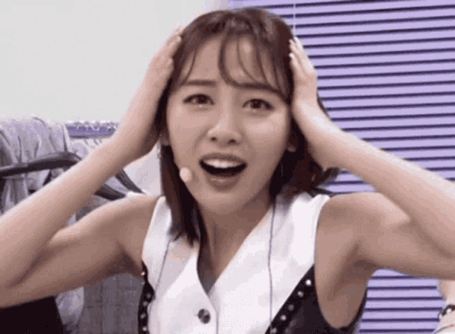 a woman is holding her head with her hands while wearing a microphone .