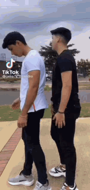 two men are standing next to each other on a sidewalk and one of them is wearing a white shirt .
