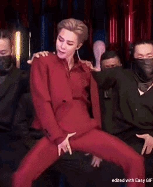 a man in a red suit is dancing in front of a group of men wearing black masks .