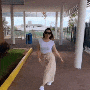 a woman is walking down a sidewalk wearing sunglasses and a white t-shirt .
