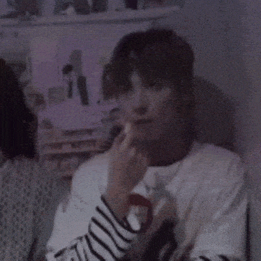a young man wearing a striped shirt and a necklace is sitting in a room .