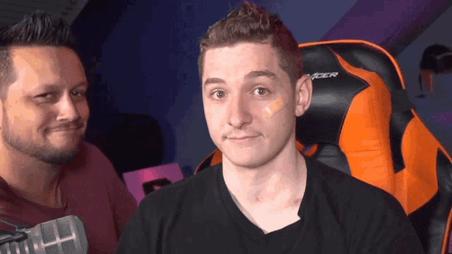 a man with a bandage on his face sits next to a racer chair