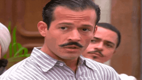a man with a mustache and a striped shirt looks at the camera