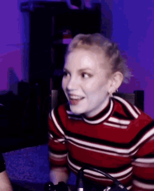 a woman in a red and white striped shirt is smiling while sitting in front of a microphone .
