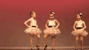 two little girls are dancing together on a stage in tutus .