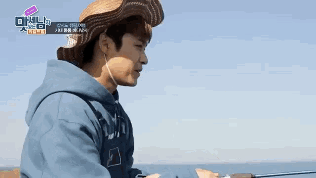 a man wearing a straw hat is holding a fishing rod in front of the ocean .
