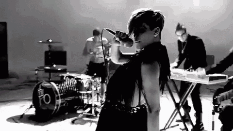 a woman is singing into a microphone in front of a drum set and keyboard .