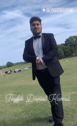 a man in a tuxedo stands in a grassy field with the name teyfik daniel kamal on the bottom right