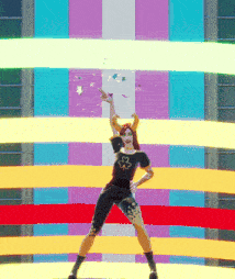 a woman with horns and a flower on her shirt stands in front of a colorful wall