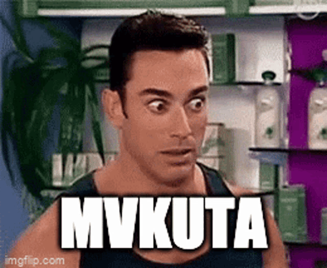 a man with a surprised look on his face is standing in front of a shelf with the word mvkuta written on it .