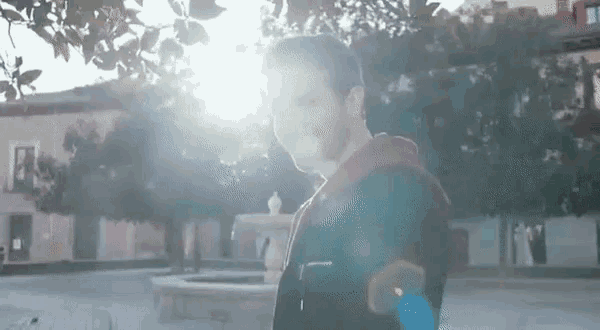 a young man is standing in front of a fountain in a park .
