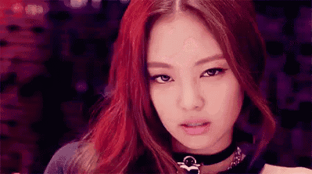 a close up of a woman with red hair wearing a choker and looking at the camera .