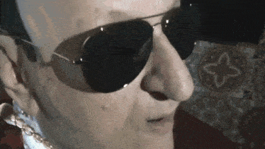 a close up of a man wearing sunglasses and a gold chain around his neck